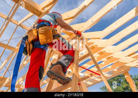 Un operaio edile sale una scala, lavorando su una struttura in legno sotto cieli azzurri, mostrando l'attività di costruzione. Foto Stock