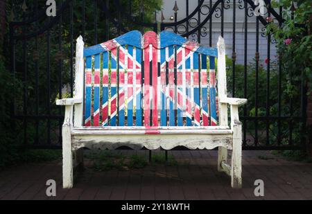 Una panchina bianca intemprata adornata con una sbiadita Union Jack siede graziosamente tra le vibranti fioriture e il verde del Giardino inglese di Yokohama, evocando un'atmosfera di Foto Stock