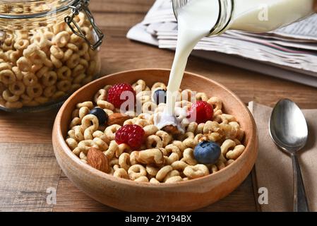 Vista dall'alto su una ciotola di cereali da colazione con mirtilli, lamponi e noci. Una bottiglia di latte viene versata nel recipiente Foto Stock