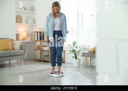 Menopausa, aumento di peso. Donna preoccupata in piedi su bilance da pavimento a casa Foto Stock