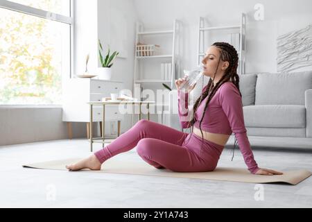 Giovane donna con dreadlocks che beve acqua dopo l'allenamento a casa Foto Stock