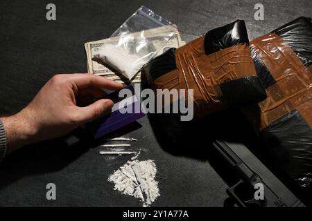 Uomo con carta di credito, pistola e pacchetti di droga su sfondo scuro, primo piano Foto Stock