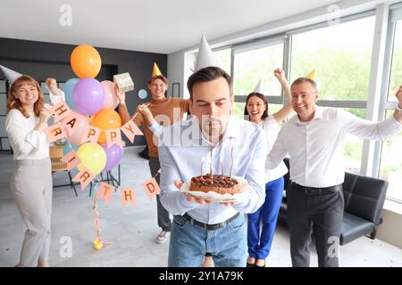 Giovane uomo d'affari che spara candele sulla torta alla festa di compleanno in ufficio Foto Stock