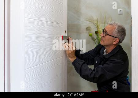 Installazione di una serratura sulla porta di legno. L'uomo prende la livella a bolla d'aria per controllare i lavori di installazione in casa Foto Stock