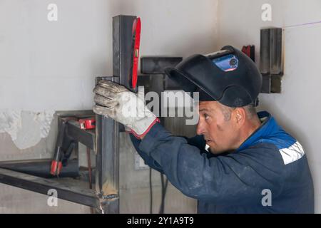 Un uomo esperto che utilizza una livella a bolla d'aria e salda una cucitura su una scala a chiocciola in un cantiere. Foto Stock