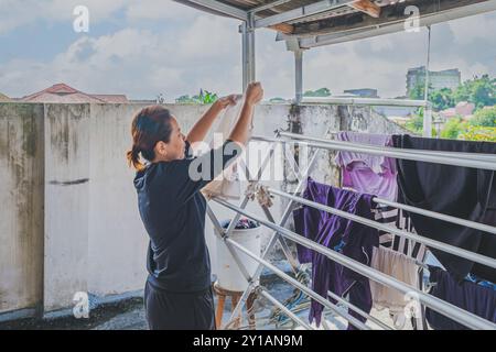 Balikpapan, Indonesia - 4 agosto 2024. Accanto a lei, un secchio pieno di vestiti attendeva il suo turno per essere appeso sulla linea. Foto Stock