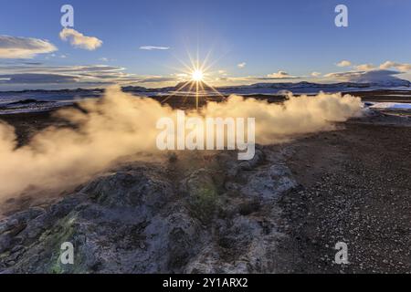 Sorgenti termali e area geotermica di fronte al paesaggio montano in inverno, raggi di sole, atmosfera nuvolosa, Hverir, Namafjall, Myvatn, Islanda, Europa Foto Stock