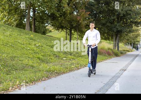 Gioioso e uomo informale equitazione scooter elettrico nel parco della città Foto Stock