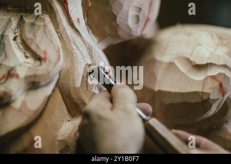 Primo piano delle mani di un artigiano usando uno scalpello per intagliare dettagli intricati in una scultura in legno Foto Stock