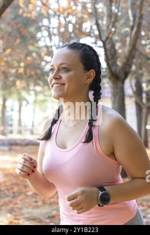 Donna sportiva sorridente che corre in un parco. Vista laterale di una ragazza atletica sorridente che corre in un parco. Giovane donna sportiva che corre in un parco Foto Stock