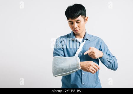 Ritratto asiatico sorridente giovane uomo che indossa un calco sul braccio rotto studio girato bianco isolato Foto Stock