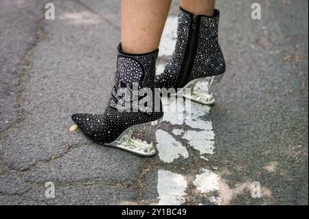 Foto di un paio a punta di stivali neri con tacco nero e paillettes di un teschio con tacco argentato in piedi su una strada incrinata. Foto Stock