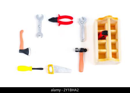 Coloratissimi strumenti giocattolo in miniatura disposti in modo creativo intorno a una cassetta degli attrezzi in legno su uno sfondo bianco. Stravagante e educativo flat-lay. Foto Stock