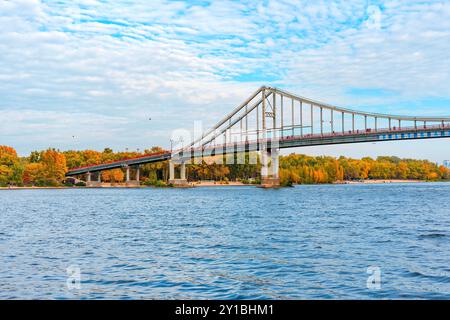 Kiev, Ucraina - 14 ottobre 2023: Ponte pedonale che attraversa il fiume Dnieper, visto dall'acqua, circondato dal fogliame autunnale a Kiev, offre panorami spettacolari Foto Stock