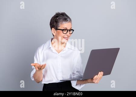 Ritratto fotografico di un bel netbook in attesa di una donna in pensione che parla di videochiamata abbigliamento formale alla moda, isolato su sfondo grigio Foto Stock