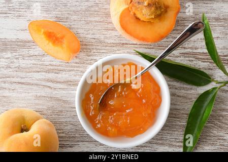 Dettaglio della marmellata di pesca in un recipiente e pezzi di frutta su un tavolo di legno. Vista dall'alto. Foto Stock