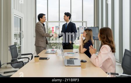 Professionista aziendale in abbigliamento formale impegnato in una stretta di mano durante una riunione in uno spazio ufficio ben illuminato. Foto Stock