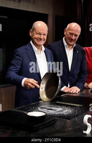 6 settembre 2024, Berlino: Il Cancelliere federale Olaf Scholz (SPD, l) si trova con Kai Wegner (CDU), sindaco di Berlino, presso lo stand AEG durante il tour di apertura nel primo giorno pubblico della fiera internazionale IFA 2024 dell'elettronica di consumo presso il centro espositivo di Berlino. Scholz trita il sale con una padella su un piano cottura resistente ai graffi di una nuova soluzione per cucina AEG con l'opzione di integrazione della casa intelligente. A settembre, circa 1.800 espositori e più di 180.000 visitatori saranno presenti al 100° anniversario della fiera leader nel settore dell'elettronica di consumo e degli elettrodomestici Foto Stock