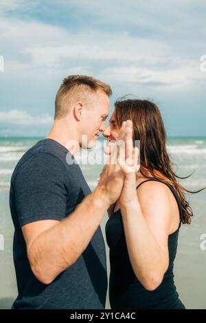 Una coppia condivide un momento intimo sulla spiaggia, tenendosi per mano Foto Stock