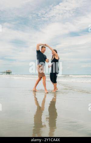 Coppia che balla sulla spiaggia, sorridendo con il riflesso sulla sabbia bagnata Foto Stock