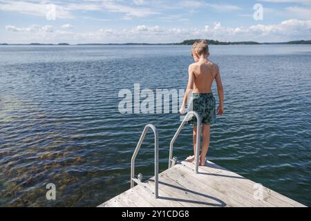 Ragazzo che contempla una nuotata dal molo di legno nel lago Foto Stock