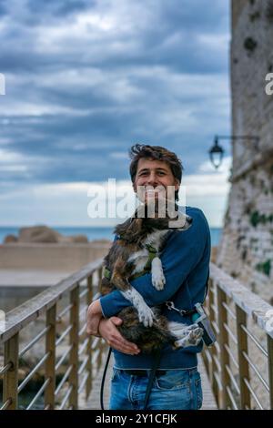 Giovane che tiene in braccio un cane marrone sorridente alla telecamera Foto Stock
