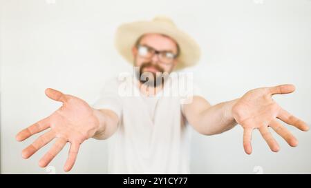 ritratto di bell'uomo barbuto con cappello di paglia e occhiali sorridenti, gesto di mano no, camicia bianca, isolata su sfondo bianco Foto Stock