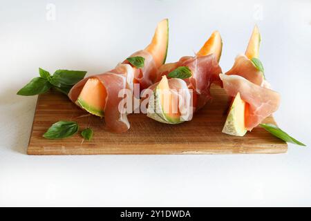 Prosciutto e melone decorati con foglie di basilico fresche isolate su sfondo bianco. Piatto estivo. Direttamente sopra. Foto Stock