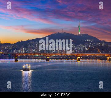 Città di Seoul dopo il tramonto e una barca turistica sul fiume Han e un ponte con il monte Namsan e la Torre di Seoul sullo sfondo, Seoul, South Kore Foto Stock