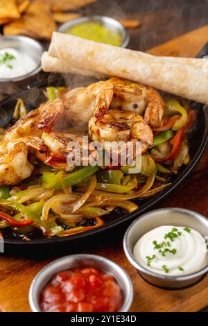 Fajitas di gamberi su un tavolo di legno con salse e tortillas a lato Foto Stock