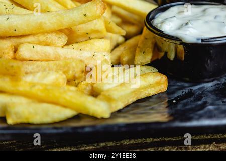 Vista ravvicinata di patatine fritte croccanti o patatine fritte, con salsa su un piatto nero Foto Stock