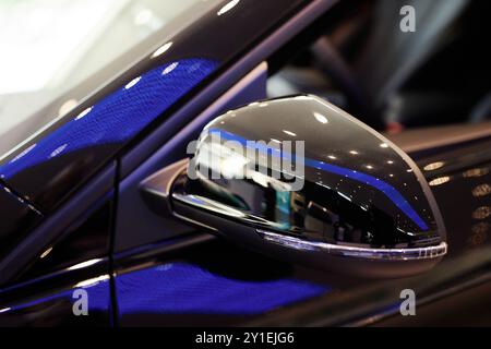 Primo piano sullo specchietto retrovisore laterale di un'auto nera pulita esposta nello showroom. Rivestimento perlescente del nuovo veicolo con riflessi sulla superficie lucida presso il centro della concessionaria, spazio di copia Foto Stock