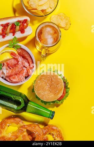 Una vivace foto che mostra la birra circondata da vari spuntini e fast food, tra cui un succoso cheeseburger, un classico hot dog e patate croccanti chi Foto Stock