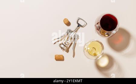 Due bicchieri da vino accanto a un cavatappi e diversi tappi di sughero, tutti disposti su uno sfondo luminoso. La luce dura crea ombre nitide, aggiungendo un effetto drammatico Foto Stock