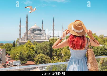 Una donna turistica di Istanbul ammira la Moschea Blu, con un gabbiano che si innalza vicino agli antichi minareti sotto il cielo estivo Foto Stock