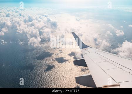Una splendida vista aerea del mare dalla finestra di un aeroplano, con l'ala che attraversa il bellissimo cielo blu e le soffici nuvole Foto Stock