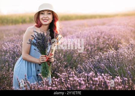 Una donna in un campo di lavanda raccoglie un bouquet fresco, godendo della bellezza della natura. Foto Stock