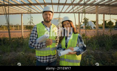 Ingegneri di successo felici lavoratori caucasici donna sorridente ragazza uomo professionale ragazzo maschio in uniforme elmetto elmetto che guarda la macchina fotografica che tiene Foto Stock