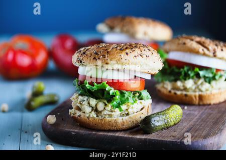 Un panino vegetariano vegano a base di ceci, lattuga, fette di pomodori freschi e cipolle con sottaceti su tutto il panino di bagel Foto Stock