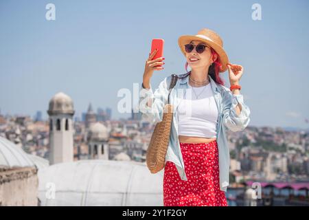 Una signora hipster a Istanbul si diverte in vacanza scattando un selfie con il suo smartphone mentre esplori le strade vivaci e le viste costiere. Foto Stock