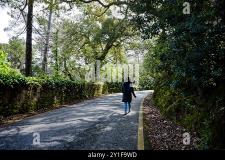 Donna che cammina lungo una stretta strada forestale mentre passa un'auto a sintra Foto Stock