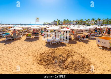 Una giornata di sole sulla spiaggia di sabbia di Playa Mogan e sul lungomare di caffetterie presso il popolare villaggio di pescatori di Puerto de Mogan, Gran Canaria, Spagna. Foto Stock