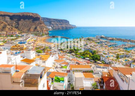 Vista panoramica dal ponte di osservazione Mirador del villaggio imbiancato, della spiaggia di sabbia, del mare blu e del porticciolo di Puerto de Mogan, Isole Canarie Foto Stock