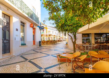 Pavimentazione portoghese con disegni tradizionali su una strada pittoresca con caffetterie e negozi sul marciapiede nella città costiera di Lagos, Portogallo. Foto Stock