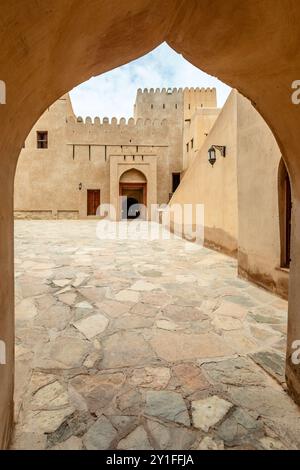 Ammira attraverso l'arco la fortezza della cittadella araba, le torri del cortile interno e le mura con la merlazione, Nizwa, il sultanato dell'Oman Foto Stock