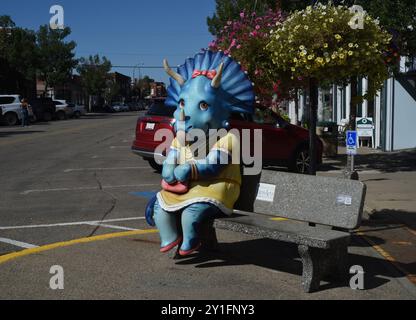 Una statua del cartone animato di una femmina di dinosauro triceratops si trova su una panchina a Drumheller, Alberta, Canada. Drumheller è noto per il suo museo paleontologico e.. Foto Stock