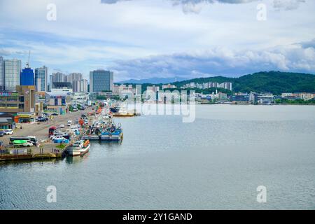 Sokcho, Corea del Sud - 28 luglio 2024: Le barche da pesca attraccate al porto di Sokcho sono allineate lungo il lungomare, con uno sfondo di edifici moderni e. Foto Stock