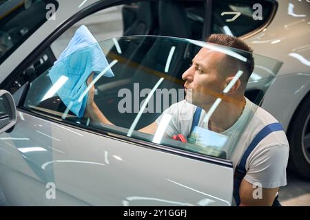 Il dipendente del servizio auto sfrega i finestrini con un tovagliolo morbido Foto Stock