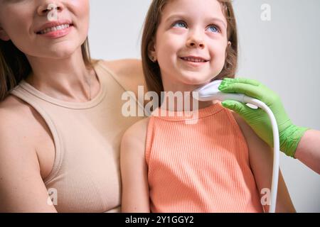 La madre che tiene la figlia come medico esegue l'ecografia del collo Foto Stock