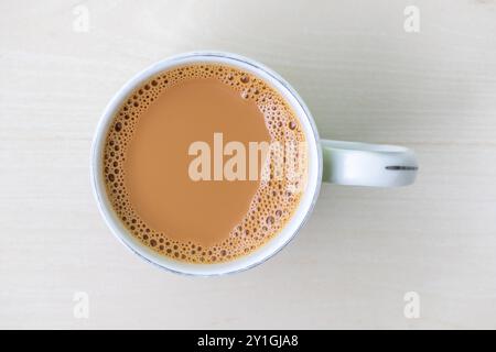 Una tazza di tè al latte o di dudh cha in una tazza di ceramica su una superficie di legno chiaro. Vista dall'alto. Foto Stock